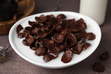 Breakfast cereal. Chocolate corn flakes and milk in bowl on brown table, closeup