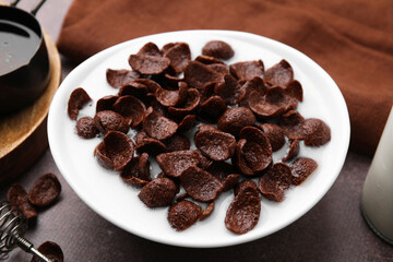 Breakfast cereal. Chocolate corn flakes and milk in bowl on brown table, closeup