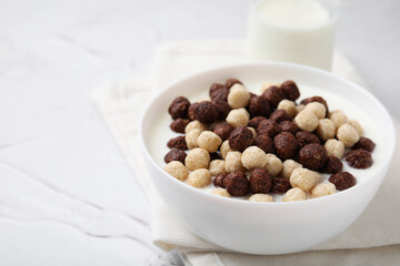 Breakfast cereal. Tasty corn balls with milk in bowl on white textured table, closeup. Space for text