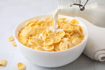 Breakfast cereal. Pouring milk into bowl with tasty corn flakes at white table, closeup