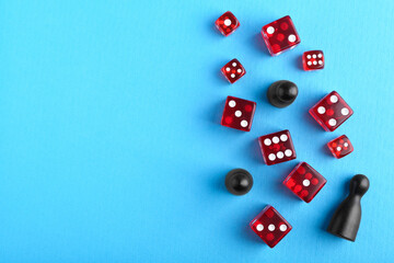 Many red dices and color game pieces on light blue background, flat lay. Space for text
