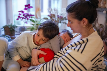 Mother cradling her newborn baby with an older child lovingly snuggling up to both of them. The...