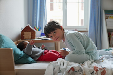 Older sibling interacting closely with a newborn baby on the bed, sharing a tender and affectionate...