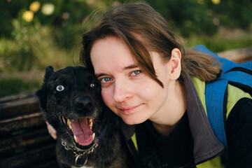 A young Caucasian woman sits on a wooden bench in a green spring park and hugs her adopted dog from...