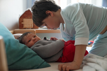 Older sibling leaning over newborn baby, observing with gentle curiosity. The soft natural light...