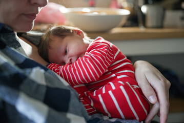 Newborn baby in red and white striped outfit snuggled up on a parent's chest, eyes closed, and...