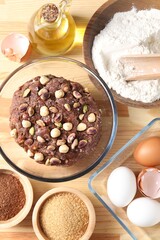 Raw chocolate dough with nuts in bowl and ingredients on wooden table, flat lay