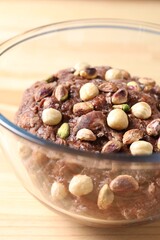 Raw chocolate dough with nuts in bowl on wooden table, closeup