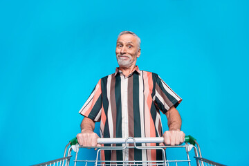 Photo of funny cheerful man wear summer striped stylish clothes walk store mall hold pushcart...