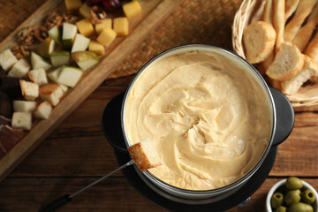 Fondue with tasty melted cheese, fork and different snacks on wooden table, top view