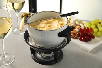 Fork with piece of apple, melted cheese in fondue pot, wine and products on grey table, closeup