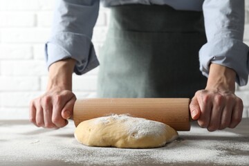 Woman rolling raw dough at table, closeup
