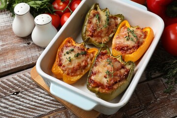 Tasty stuffed peppers in dish and ingredients on wooden table