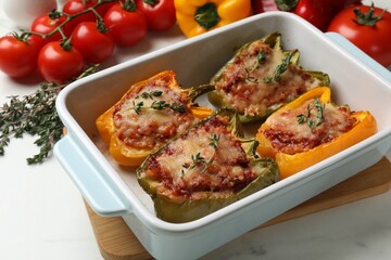 Tasty stuffed peppers in dish and ingredients on white table