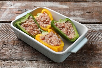 Raw stuffed peppers in dish on wooden table