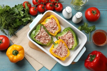Raw stuffed peppers in dish and ingredients on wooden table, flat lay
