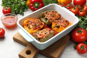 Tasty stuffed peppers in dish and ingredients on grey table