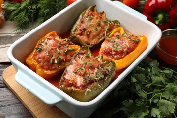 Tasty stuffed peppers in dish and ingredients on wooden table, closeup