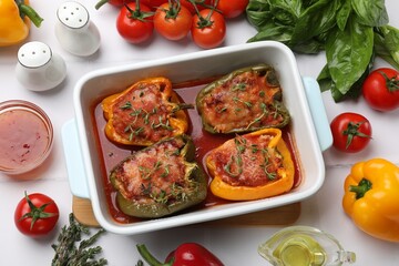 Tasty stuffed peppers in dish and ingredients on white tiled table, flat lay