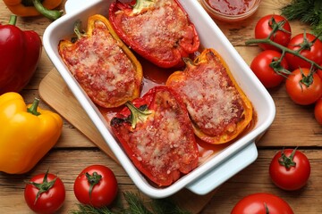 Tasty stuffed peppers in dish and ingredients on wooden table, flat lay