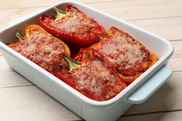 Tasty stuffed peppers in dish on light wooden table, closeup