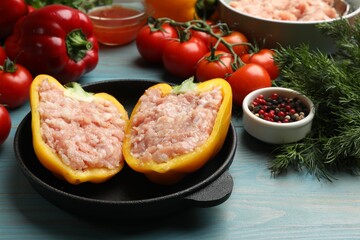 Raw stuffed peppers with ground meat and ingredients on light blue wooden table