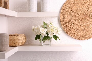 Beautiful jasmine flowers in vase and decor on shelves indoors