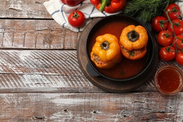 Tasty stuffed peppers in pan, sauce and products on wooden rustic table, flat lay. Space for text