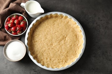 Making shortcrust pastry. Raw dough in baking dish, milk, sugar and strawberries on grey table, top...