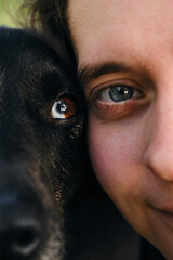 Blue eyed woman and black heterochromia eyed dog close up in a natural setting. Half of girls face...