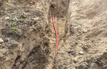 The red wire lies in a trench among soil, grass and stones. Sewer line repair.