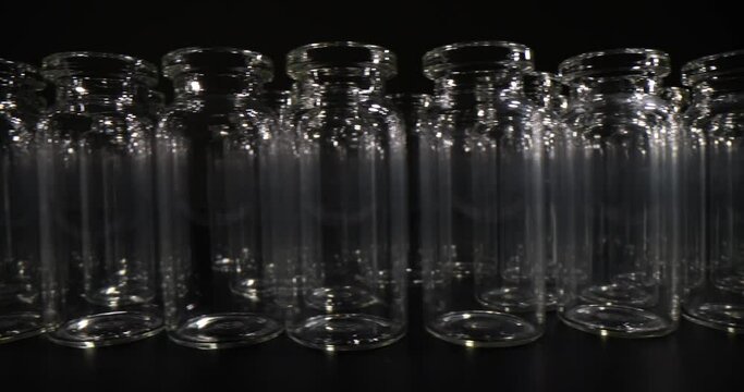 Transparent glass vials for vaccines standing in long row on dark table. Glassware for laboratory and medical purposes on black background