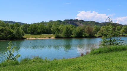 Lac du chanoine Kir, à Dijon, en Côte d’Or / Bourgogne, paysage de nature verte avec des arbres et une pelouse au bord de l’eau, sous un ciel bleu, au printemps (France)