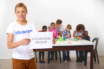 Volunteers needed, portrait or child with sign for donation, help or paper for community service or society. Charity, teen or happy boy with poster at non profit ngo orphanage for support or youth