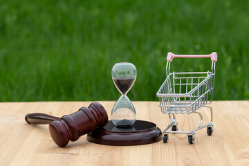 Hourglass, judge's gavel and miniature shopping cart from a supermarket on a wooden surface