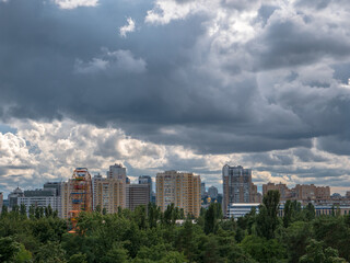 Obraz premium Low sky with dark cumulus storm thunder clouds above the high-rise buildings, observation wheel, dome church and Peremohy park in Kyiv (Kiev) city. Rainy weather concept.