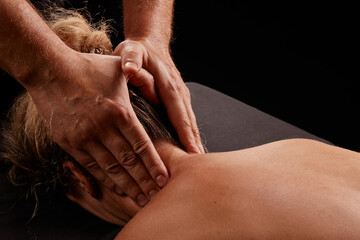 a male masseur massages a girl's neck on a dark background, neck massage