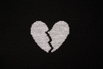 Broken heart is embroidered with white threads on black fabric. 