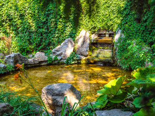 Intimate cosy atmosphere in a park with waterfall fountain buried in crawling plants.