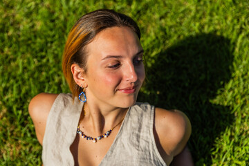A woman is laying on the grass and wearing a necklace smiling, photo with copy space