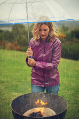 Outdoor, woman and rain at barbecue with umbrella, frustrated and sad in yard or at fire in Glasgow. Female person, grill and bbq in bad weather with burning, flame and wind in backyard in Scotland
