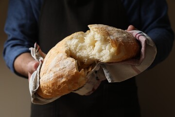 Man breaking loaf of fresh bread on dark background, closeup