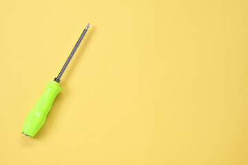 Screwdriver with green handle on light yellow background, top view. Space for text