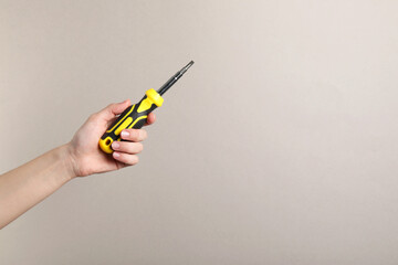 Woman holding screwdriver on grey background, closeup. Space for text