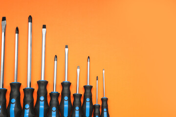 Set of screwdrivers on orange background, flat lay. Space for text