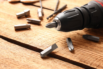 Electric screwdriver with bit set on wooden table, closeup