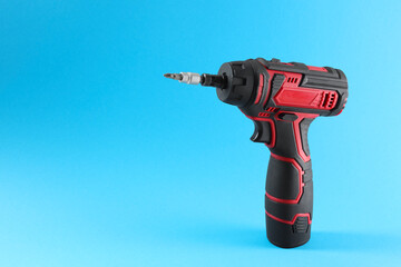 Modern electric screwdriver on light blue background. Space for text