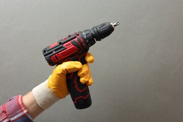Handyman holding electric screwdriver on grey background, closeup