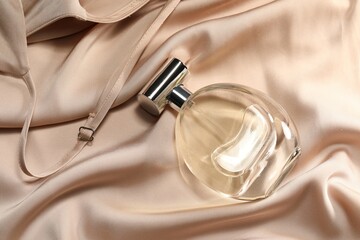 Luxury perfume in bottle on beige silk fabric, top view
