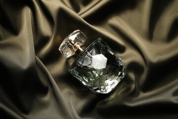Luxury perfume in bottle on dark silk fabric, top view